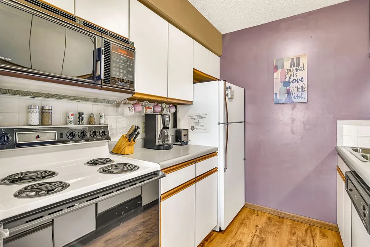 A section of the kitchen highlighting the stove, refrigerator, coffee maker, and decorative wall art. The setup is homey and practical, emphasizing the kitchen’s readiness for any meal, from quick snacks to elaborate feasts.