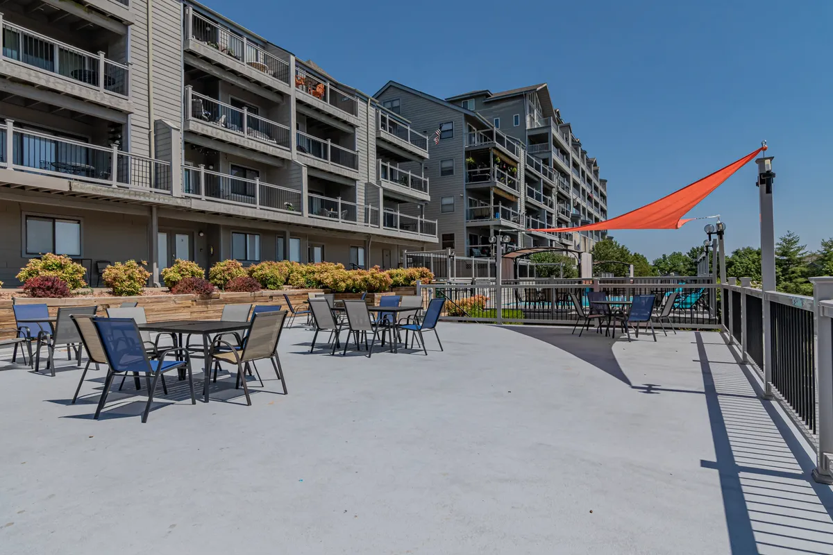 This vibrant exterior shot features a communal outdoor seating area shaded by a bright orange sail, surrounded by colorful flower beds and the balconies of the condo building. The space is designed for lively social gatherings, outdoor dining, and relaxation.