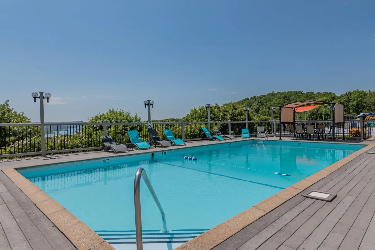 An inviting swimming pool surrounded by lounge chairs and a shaded canopy area, with lush landscaping in the background. The pool is easily accessible and appears close to the condo, suggesting convenience for guests of all ages who want a refreshing swim or a place to relax in the sun.