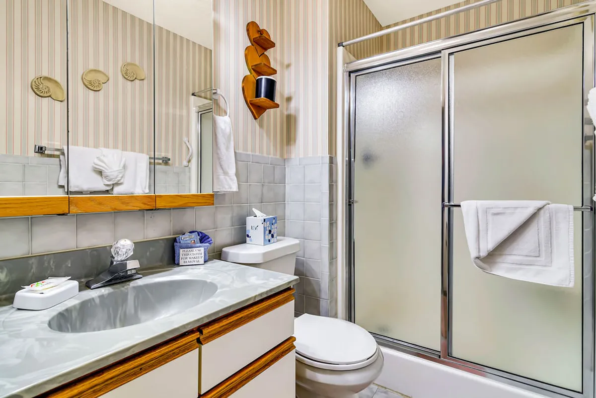 A well-appointed bathroom with a sink featuring a marble countertop, a framed mirror, a spacious shower stall, and tasteful wooden wall decor. The space feels calm and refreshing, perfect for morning or evening routines.