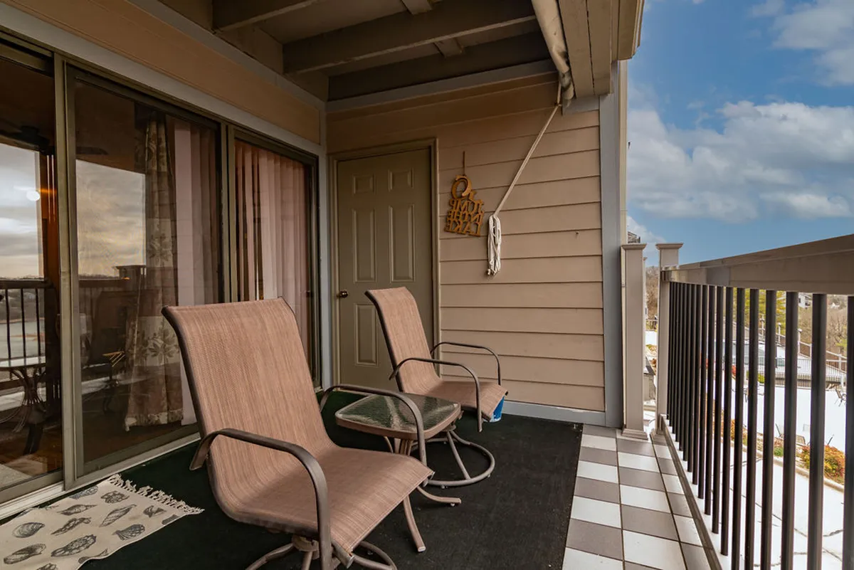 A serene patio area with two chairs and a small glass table adjacent to a sliding glass door, overlooking scenic outdoor views. The setup is simple and accessible, allowing guests to relax, read, or enjoy the view—morning light gently streams in, enhancing the peaceful atmosphere.