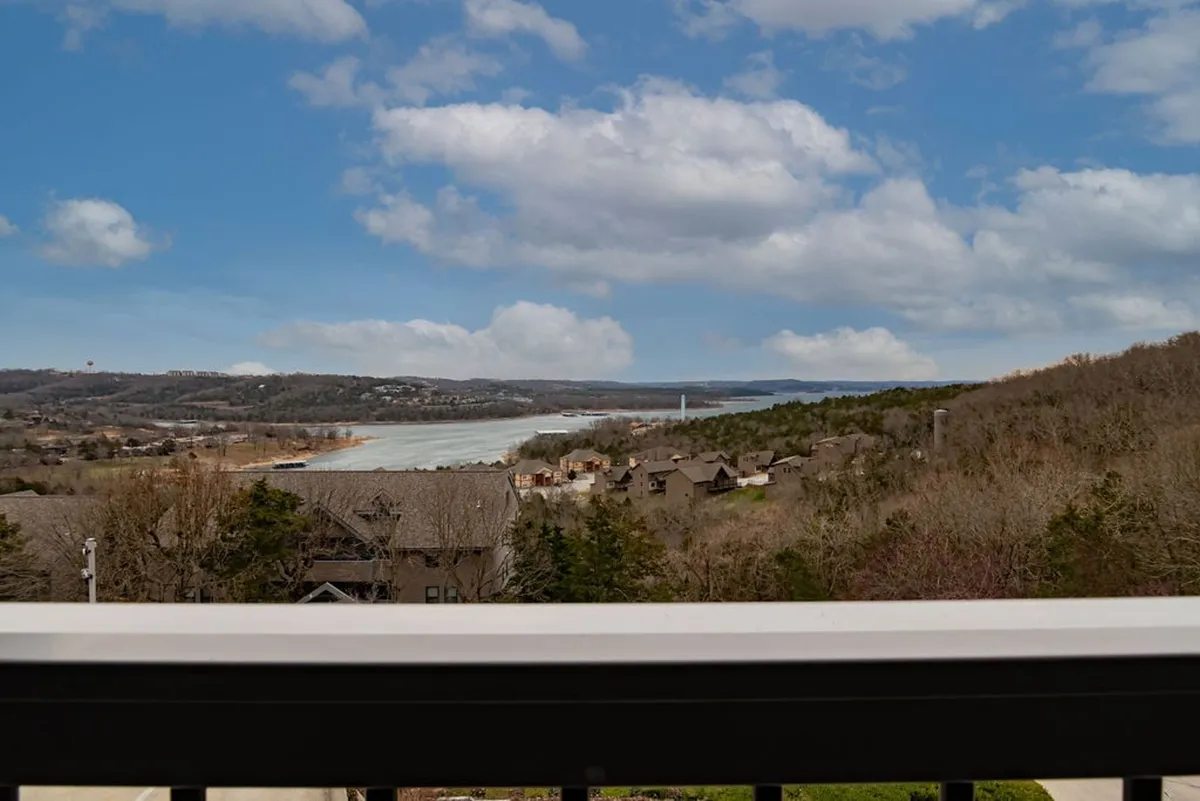 The image showcases a tranquil panoramic view over a serene river winding through rolling hills, all beneath a dramatic cloudy sky. The scene invites relaxation, with natural beauty and the promise of outdoor activities like hiking, fishing, and picnicking. The vantage point suggests the view is easily accessible from the condo's deck, further enhancing the sense of peace and connection to nature.