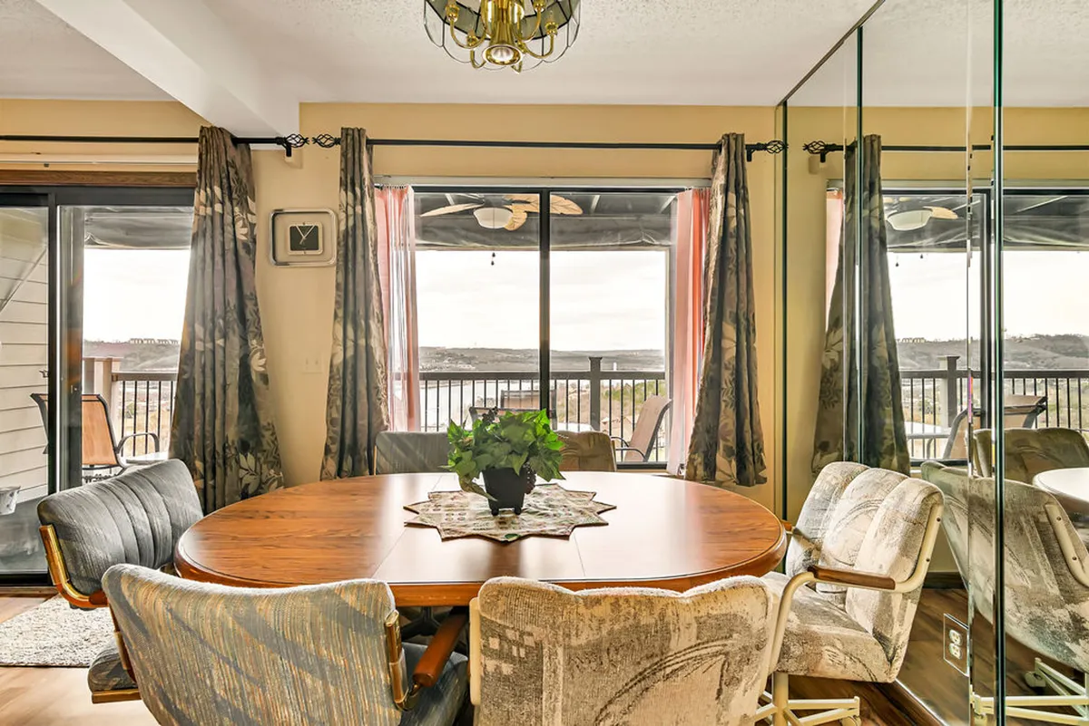 A round wooden dining table set near expansive windows, accented by a decorative plant centerpiece and a mirrored wall. The space is ideal for family dinners, social gatherings, and enjoying scenic sunset views over the water.